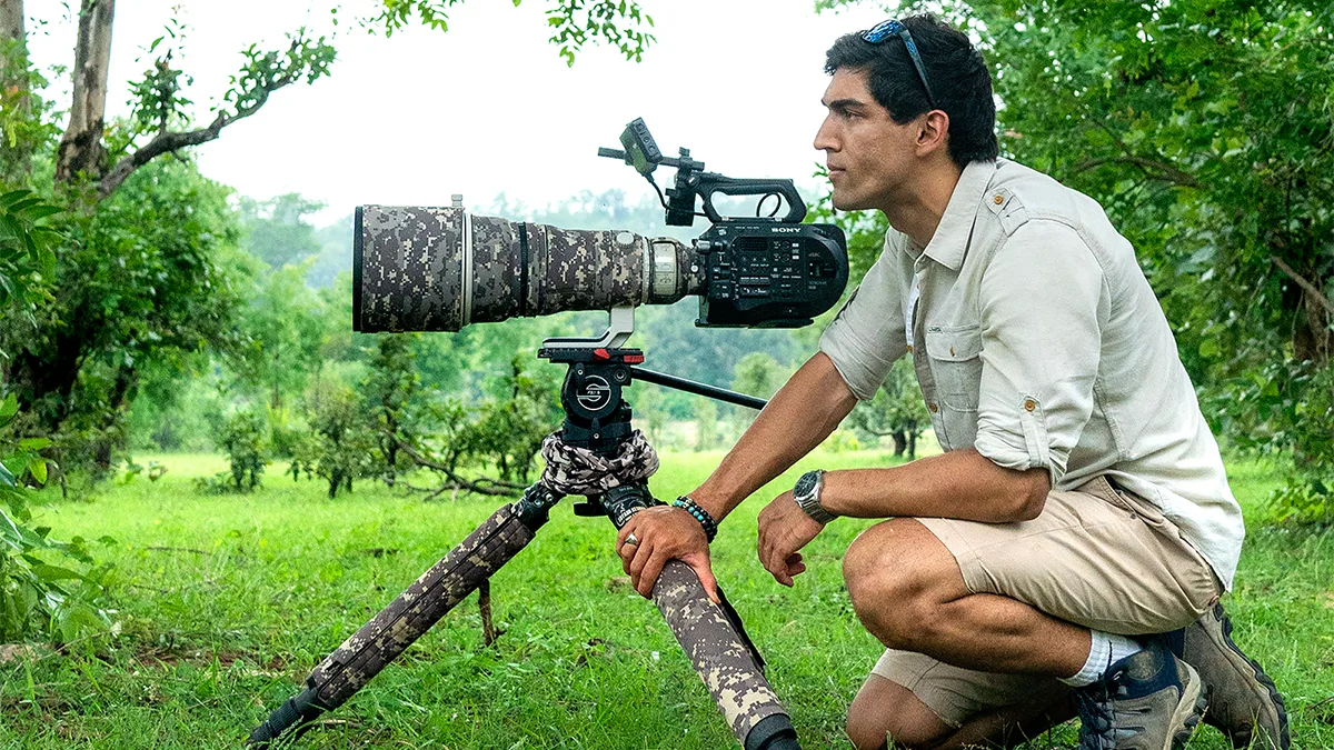 Suyash Keshari crouched beside a long-lens camera on a tripod in a green meadow