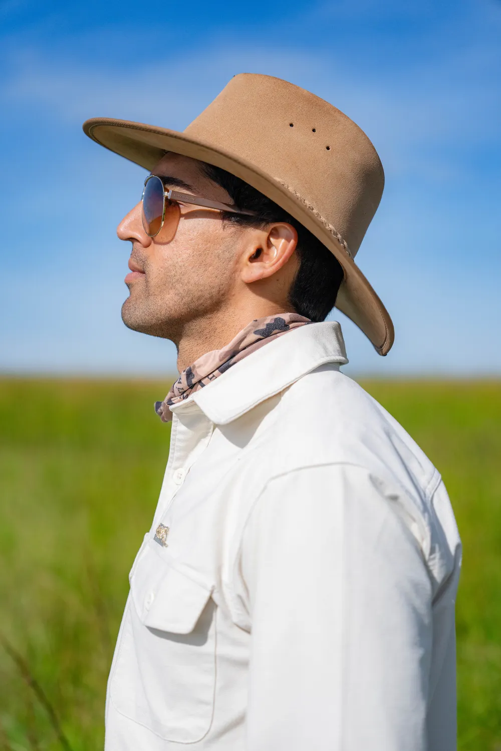 Suyash Keshari in profile, wearing a hat and sunglasses, grassland behind him